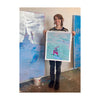 Alissa McKendrick holding her print, Untitled, in front of her body while standng in front of a large painting propped up on a plastic bucket.
